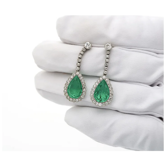 Pair of emerald earrings on a white surface with a white glove.