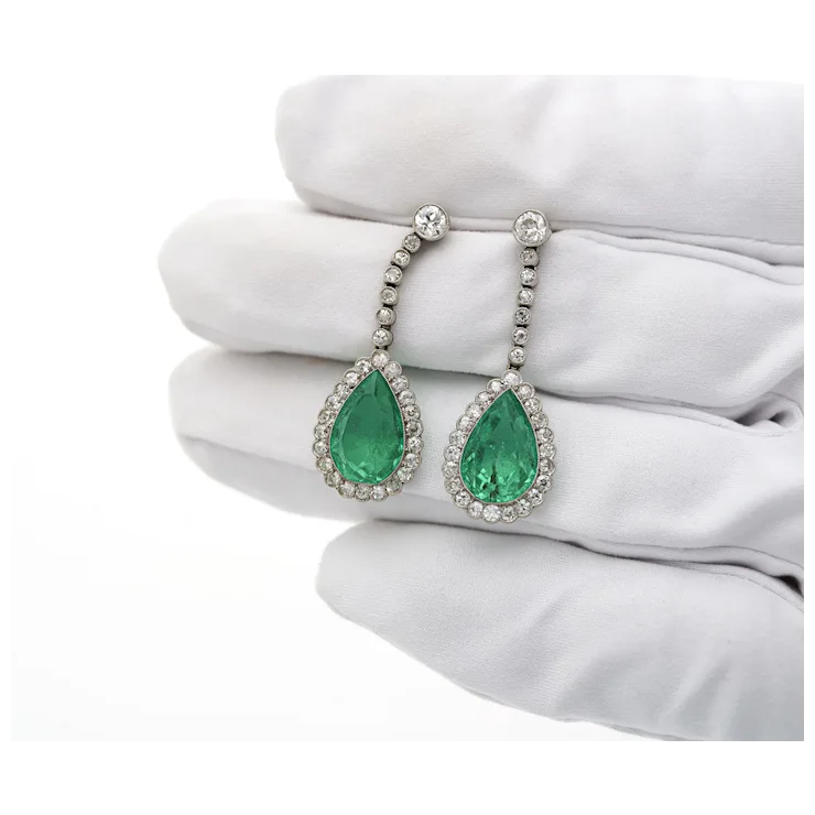 Pair of emerald earrings on a white surface with a white glove.