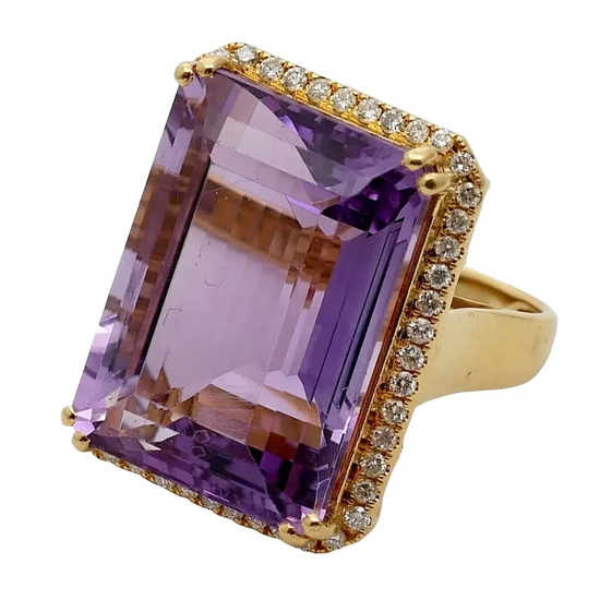 Gold ring with a large purple gemstone and smaller diamonds on a white background
