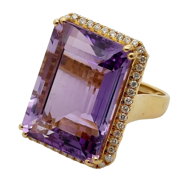 Gold ring with a large purple gemstone and smaller diamonds on a white background