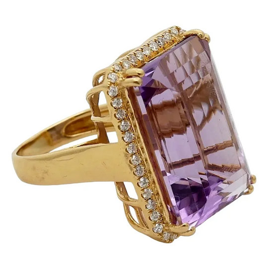 Gold ring with a large purple gemstone and smaller diamonds on a white background