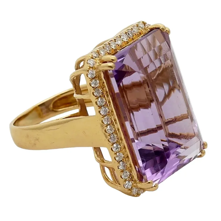 Gold ring with a large purple gemstone and smaller diamonds on a white background
