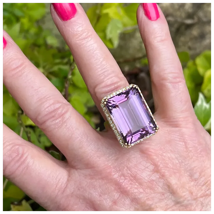 Hand wearing a ring with a purple gemstone against a blurred green background