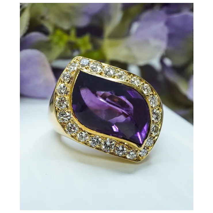 Gold ring with a purple gemstone on a white surface with blurred flowers in the background