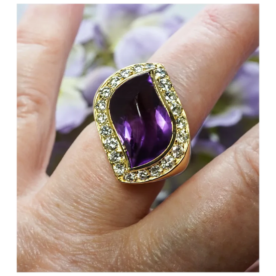 Gold ring with a purple gemstone on a finger against a blurred floral background