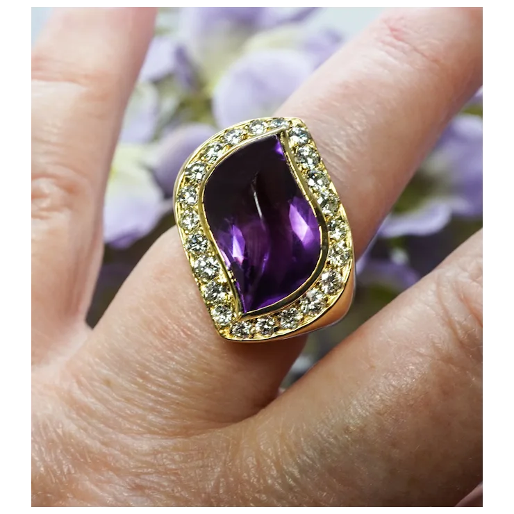 Gold ring with a purple gemstone on a finger against a blurred floral background