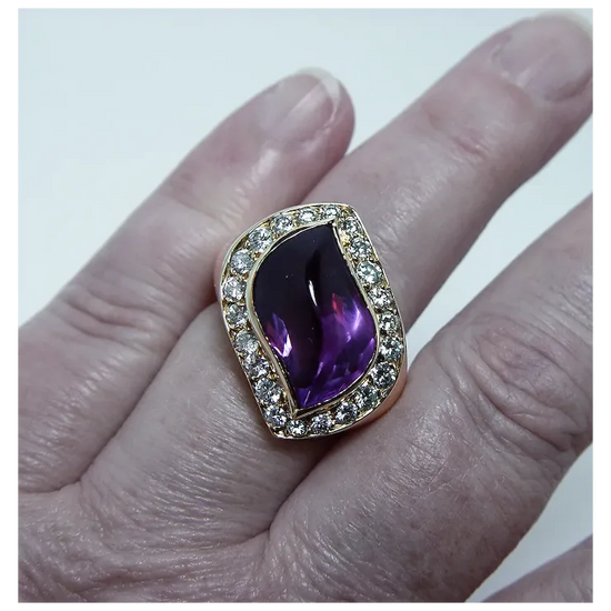Ring with a purple gemstone and diamond accents on a finger against a white background