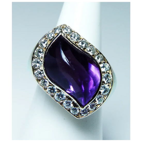 Ring with a purple teardrop-shaped gemstone and diamond-studded band on a white background