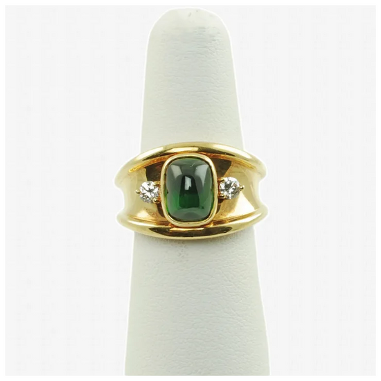 Gold ring with a green gemstone and diamonds on a white cushion