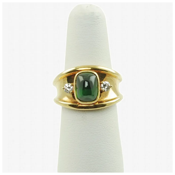 Gold ring with a green gemstone and diamonds on a white cushion