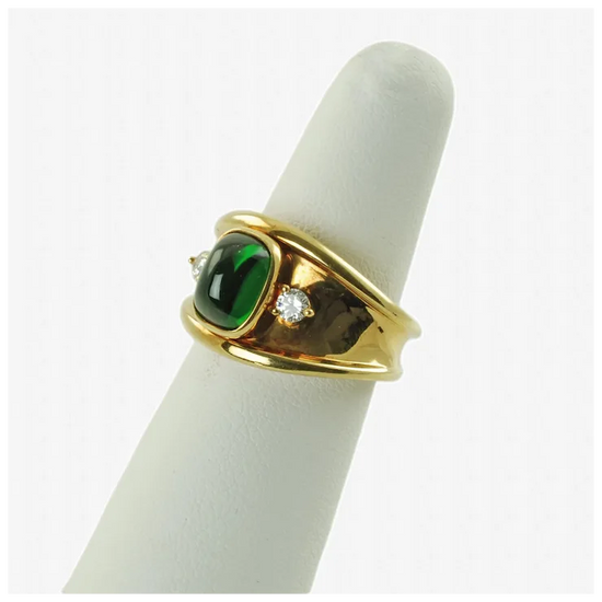 Gold ring with green gemstone and diamond on a white cylindrical stand