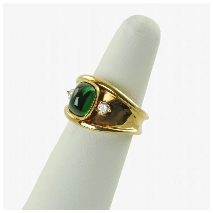 Gold ring with green gemstone and diamond on a white cylindrical stand