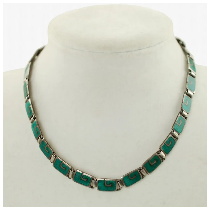 Necklace with green and silver design on a mannequin bust against a white background