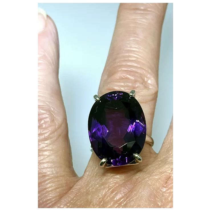 Ring with a purple gemstone on a person's finger against a light blue background